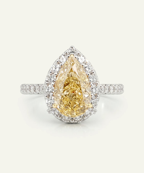 Teardrop-shaped yellow diamond ring with a white gold band on a light gray background