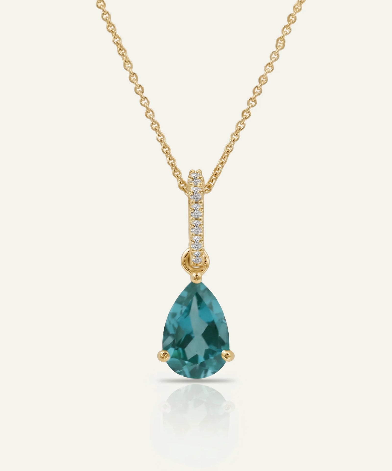 Gold necklace with a green teardrop pendant on a white background