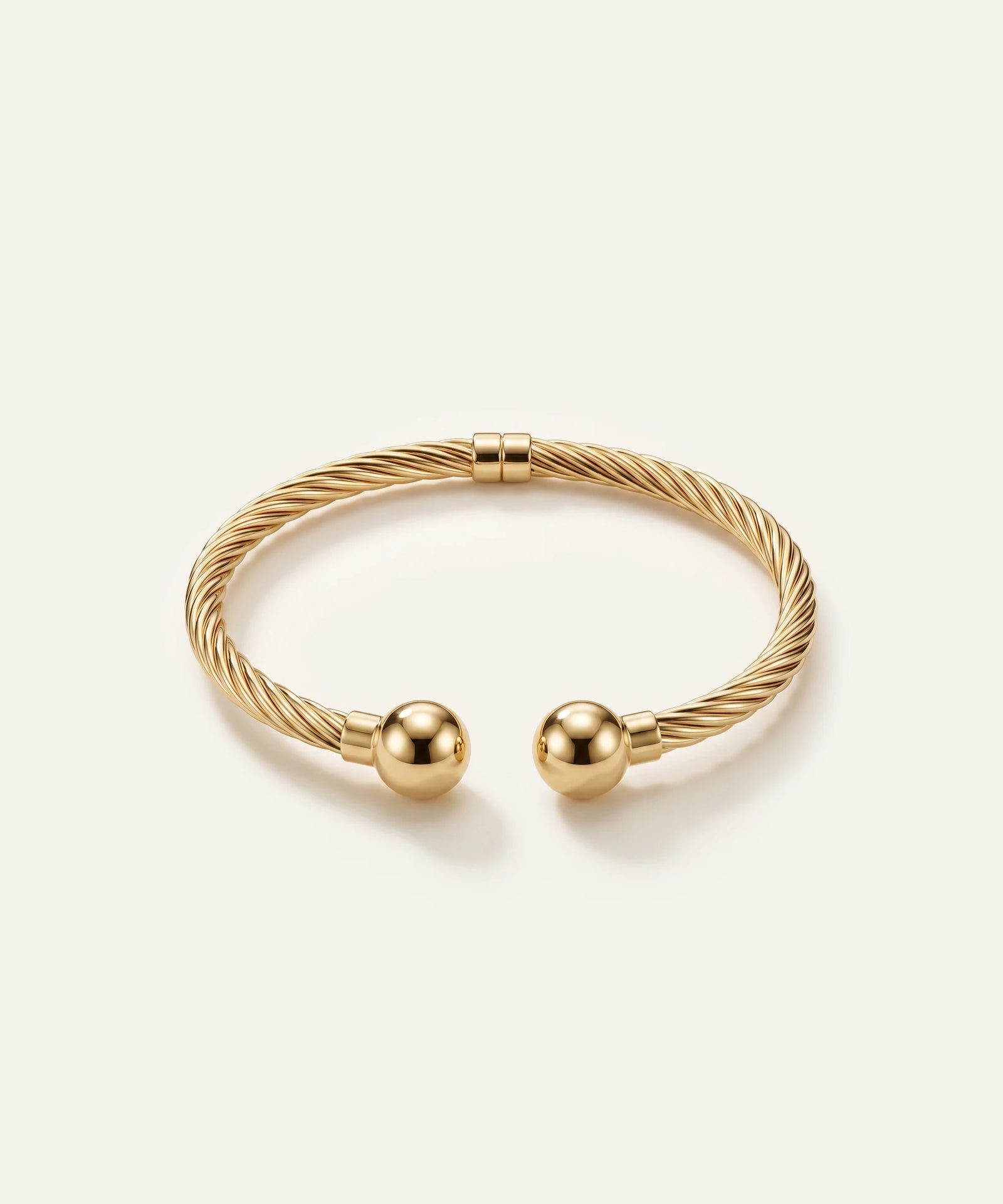 Gold bracelet with two spherical charms on a light beige background