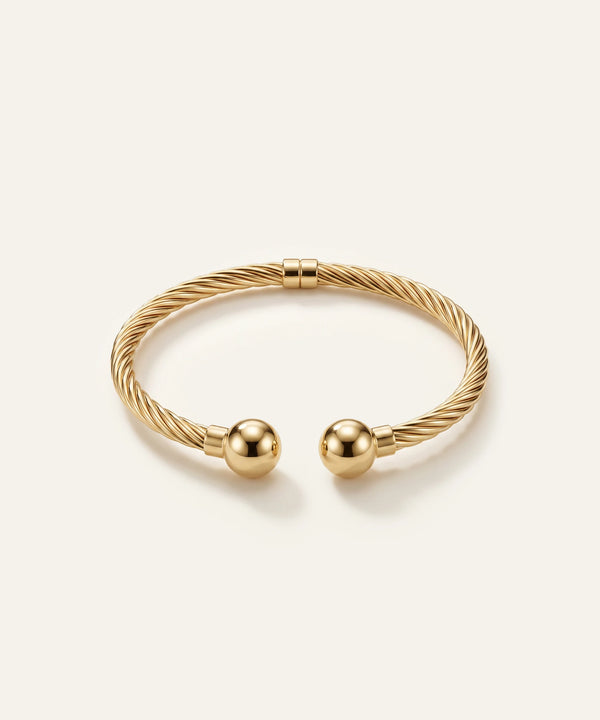 Gold bracelet with two spherical charms on a light beige background