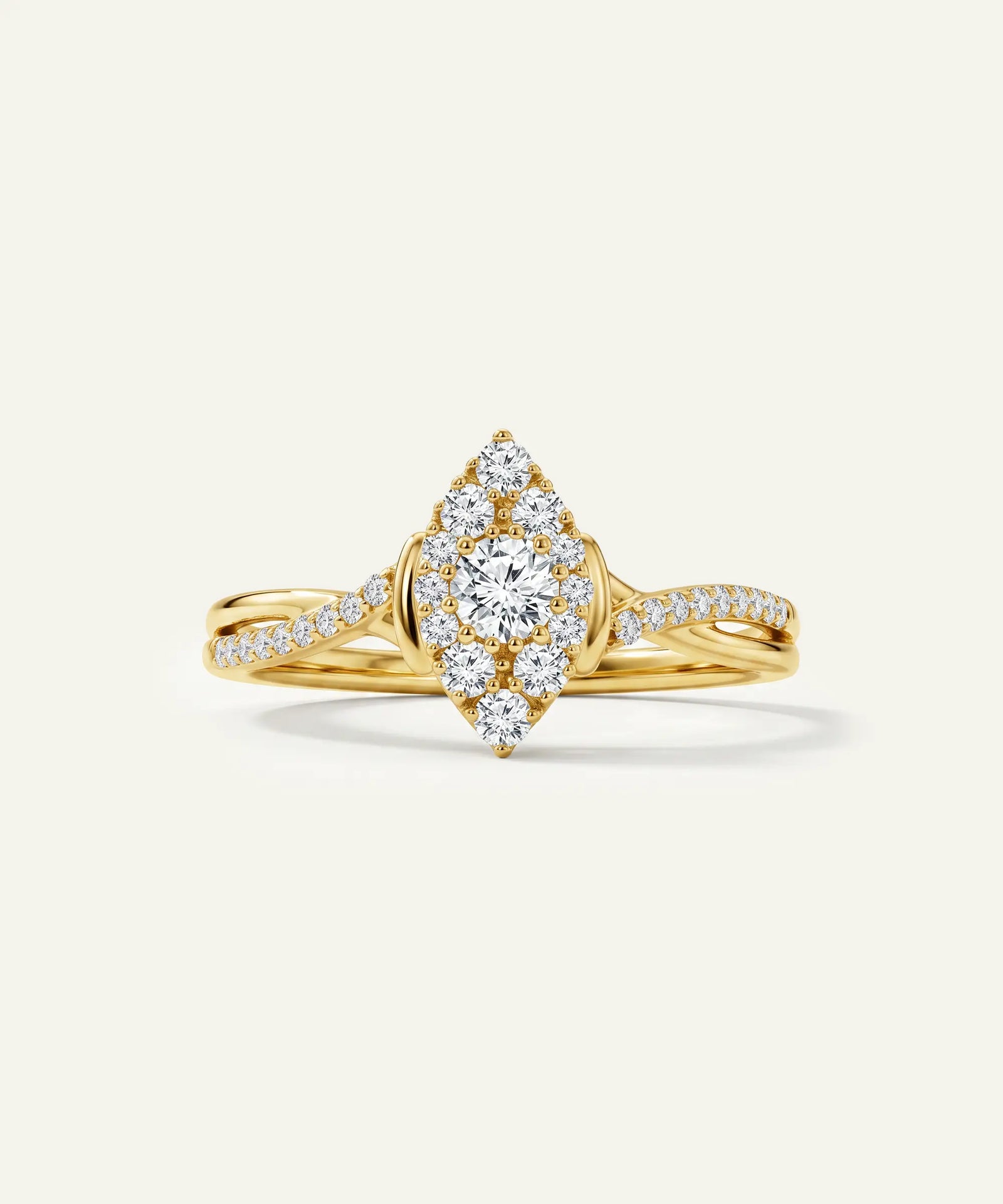 A yellow gold diamond ring with a marquise-shaped cluster setting featuring a round center diamond and smaller surrounding diamonds, set on a twisted shank with pavé diamonds, photographed on a light cream background.