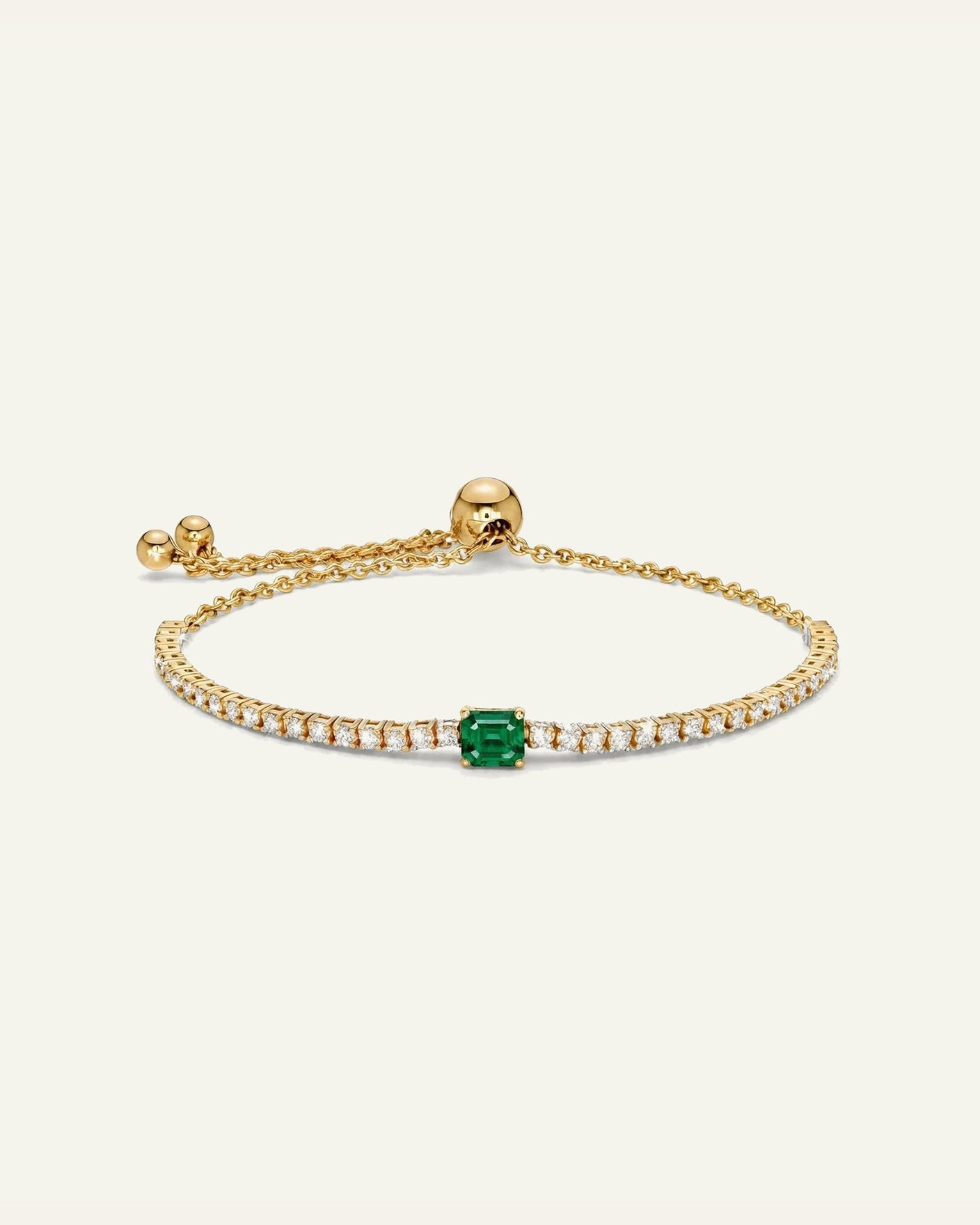 A delicate gold chain bracelet featuring a central emerald-cut green gemstone pavé-set with small clear stones, shown on a light cream background.