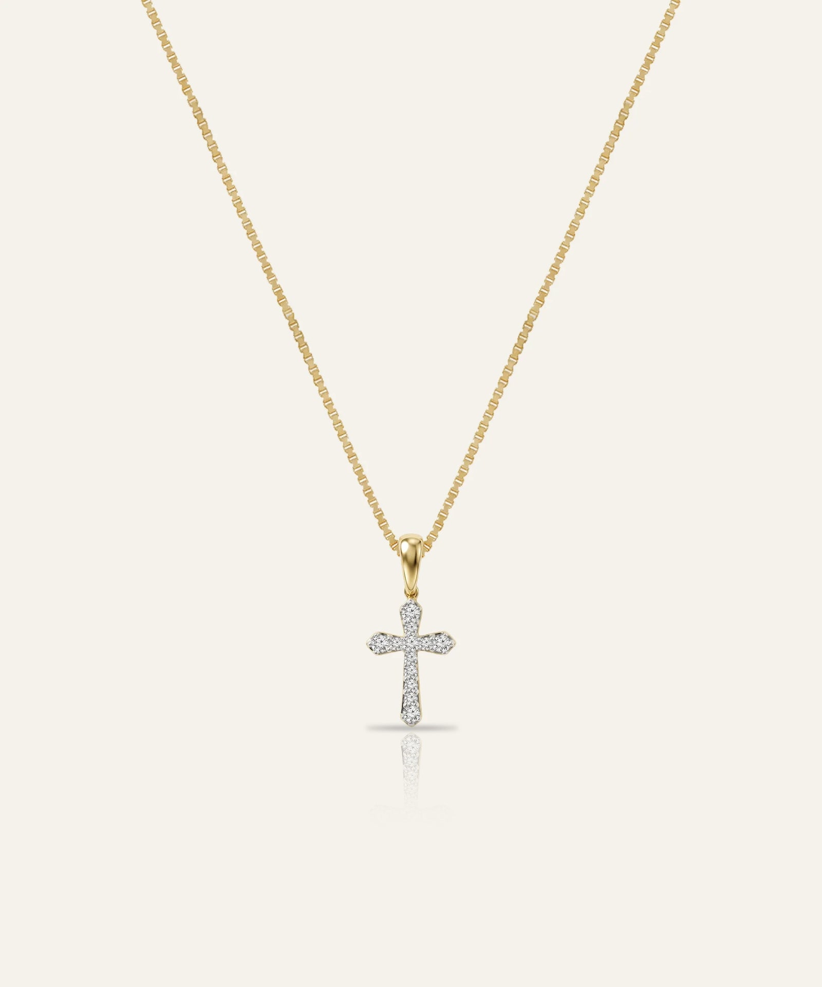 Gold necklace with a diamond cross pendant on a light beige background