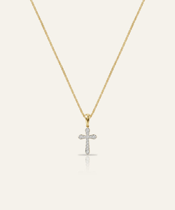 Gold necklace with a diamond cross pendant on a light beige background