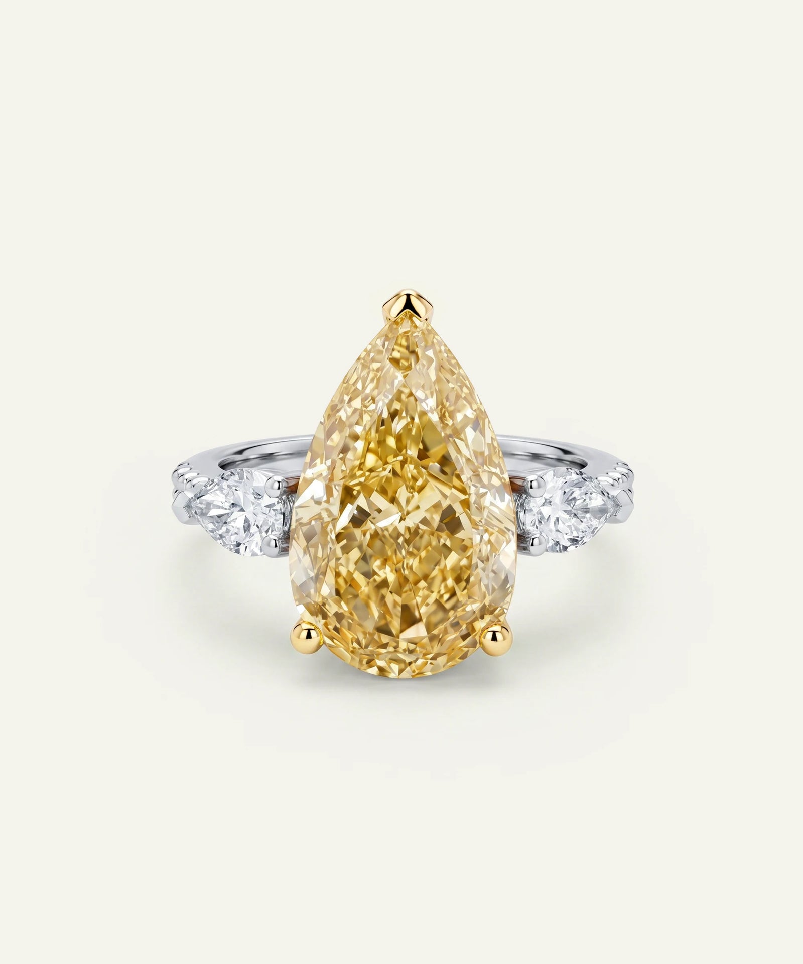 Pear-shaped fancy yellow diamond engagement ring set in yellow gold prongs, accented by round brilliant-cut white side diamonds on a white metal band. The ring is displayed from the front against a light neutral background.