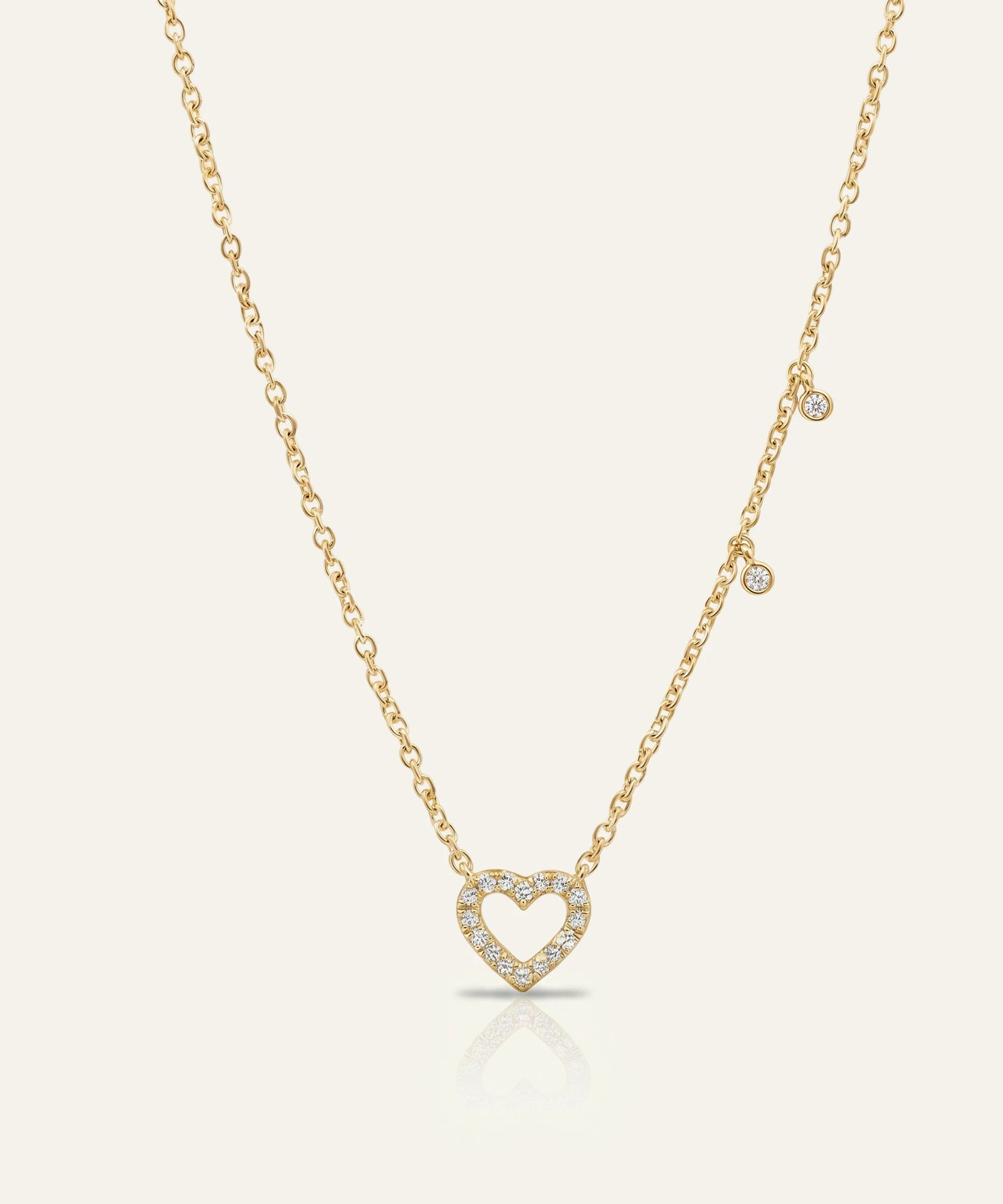 Gold necklace with a heart-shaped pendant on a light beige background