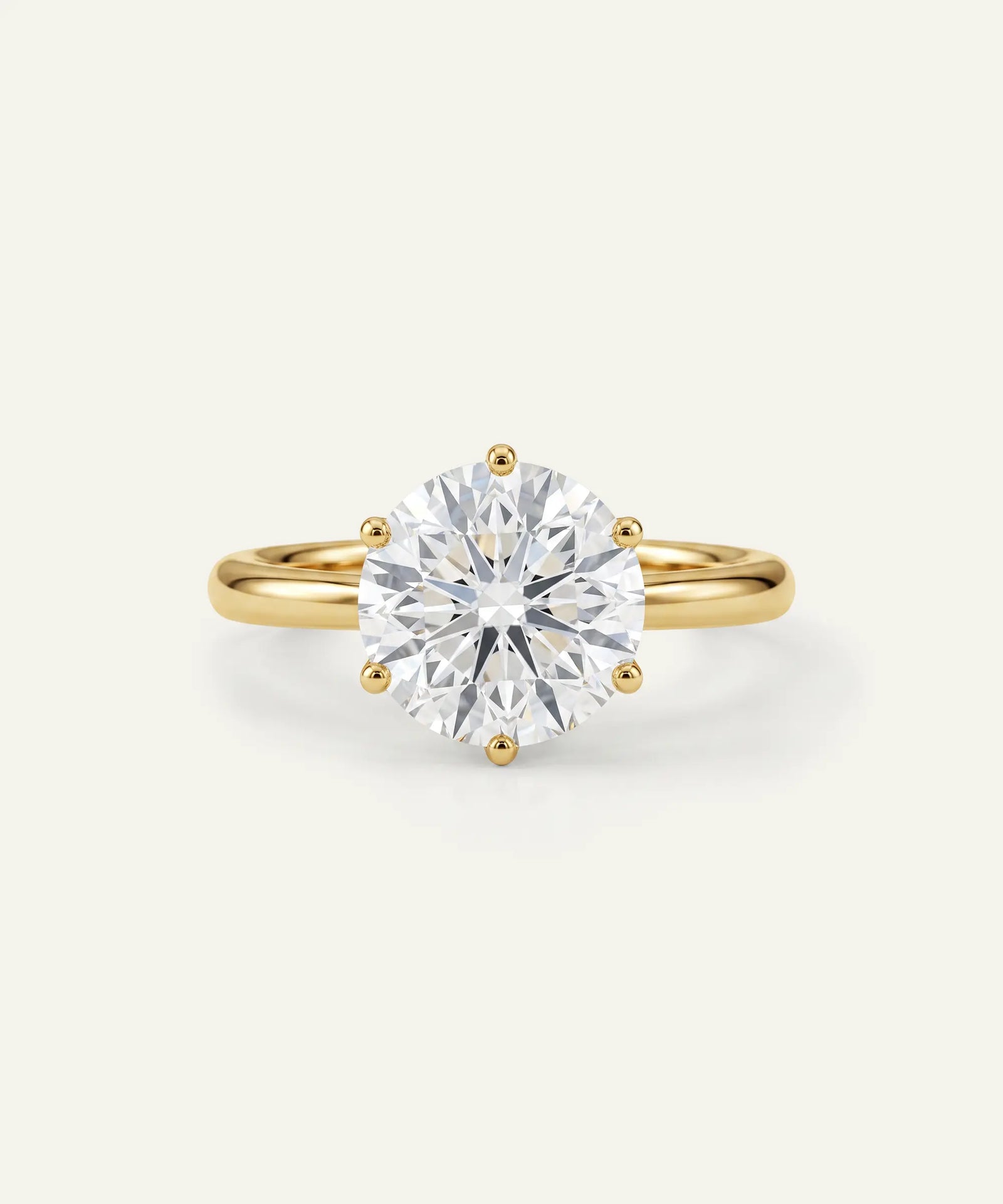A yellow gold solitaire engagement ring featuring a round brilliant-cut diamond center stone in a prong setting, shown on a clean off-white background.
