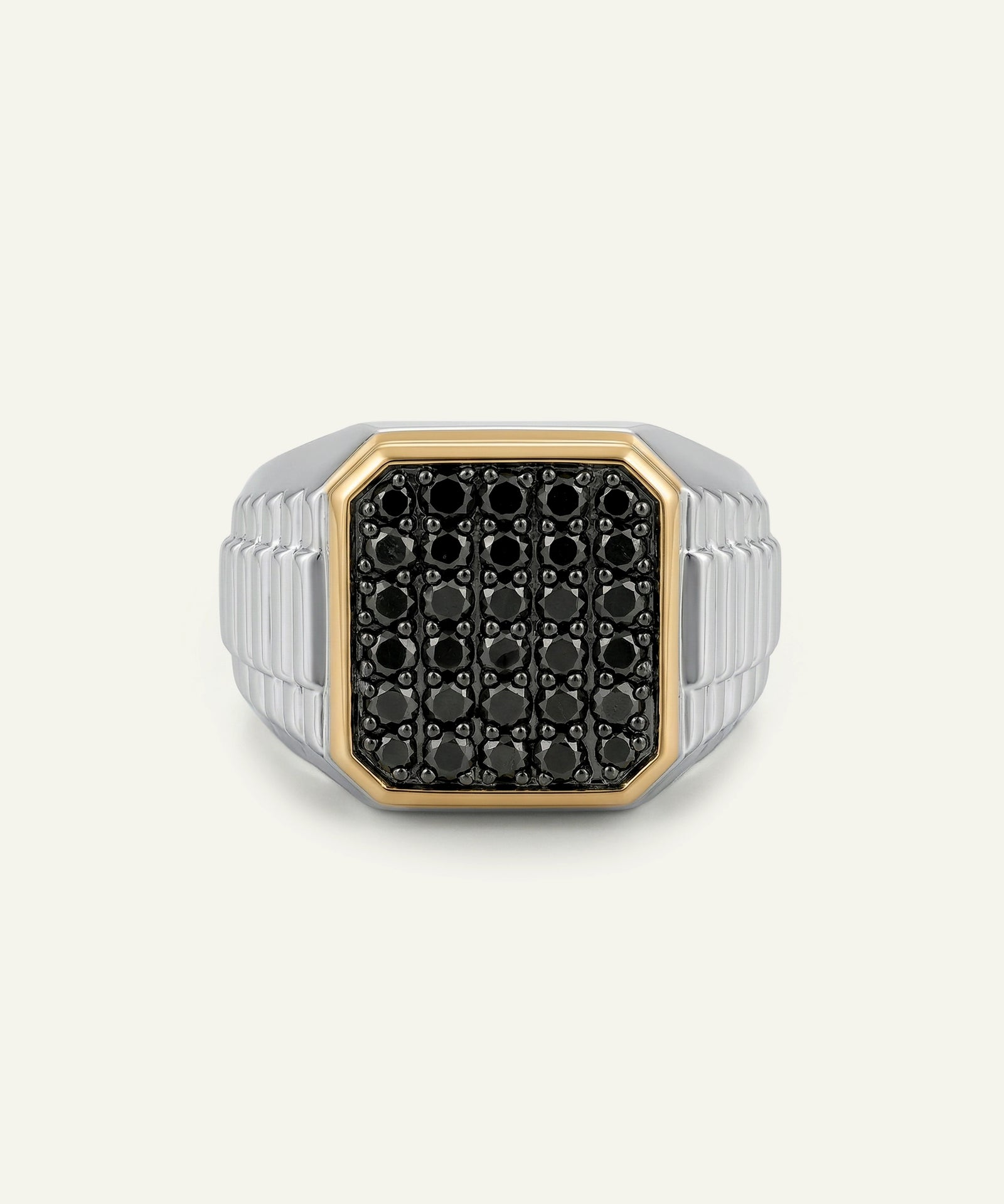 A men's signet ring featuring a black pavé face with a gold bezel, set on a silver-toned ribbed band, shown against a light off-white background.