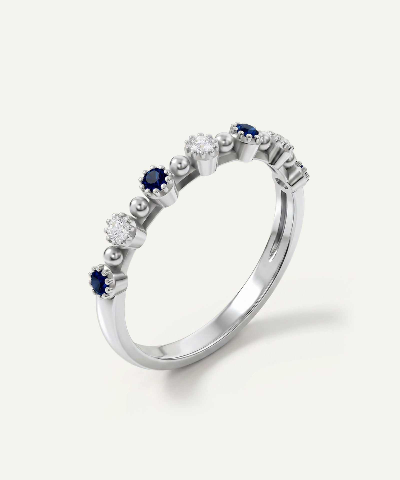 A silver-tone eternity ring featuring alternating round-cut dark blue sapphires and clear round diamonds, set on a clean off-white background.