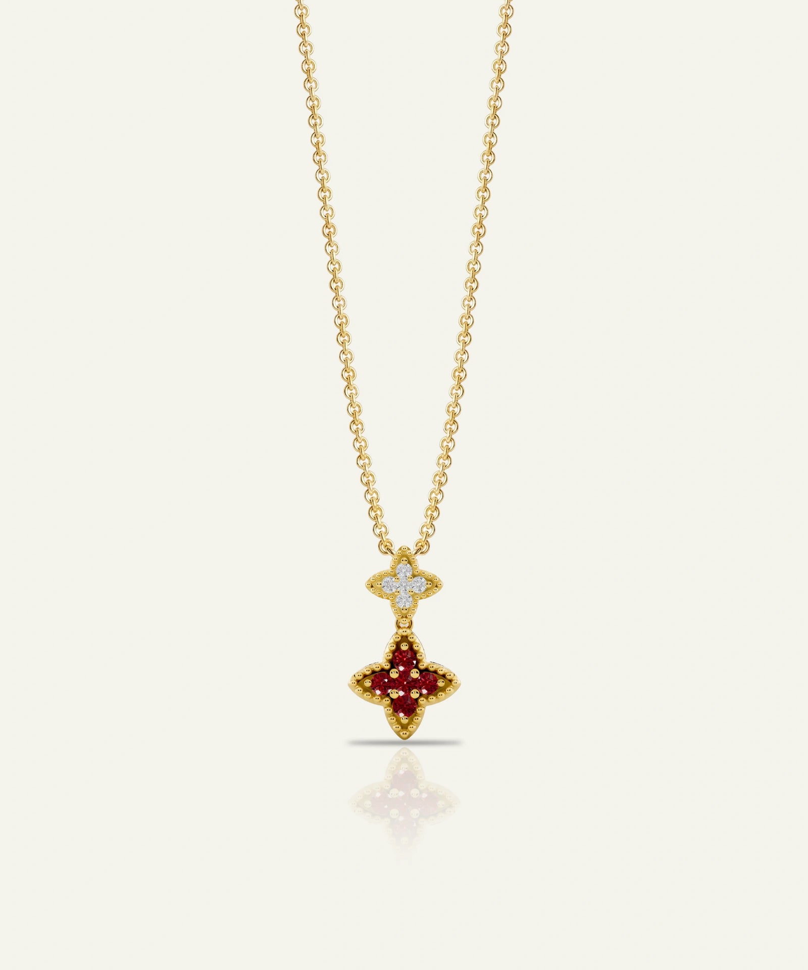A gold chain necklace with a double-pendant design, featuring a small diamond-encrusted cross at the top and a larger gold cross pendant set with deep red gemstones below, shown on a light cream background.