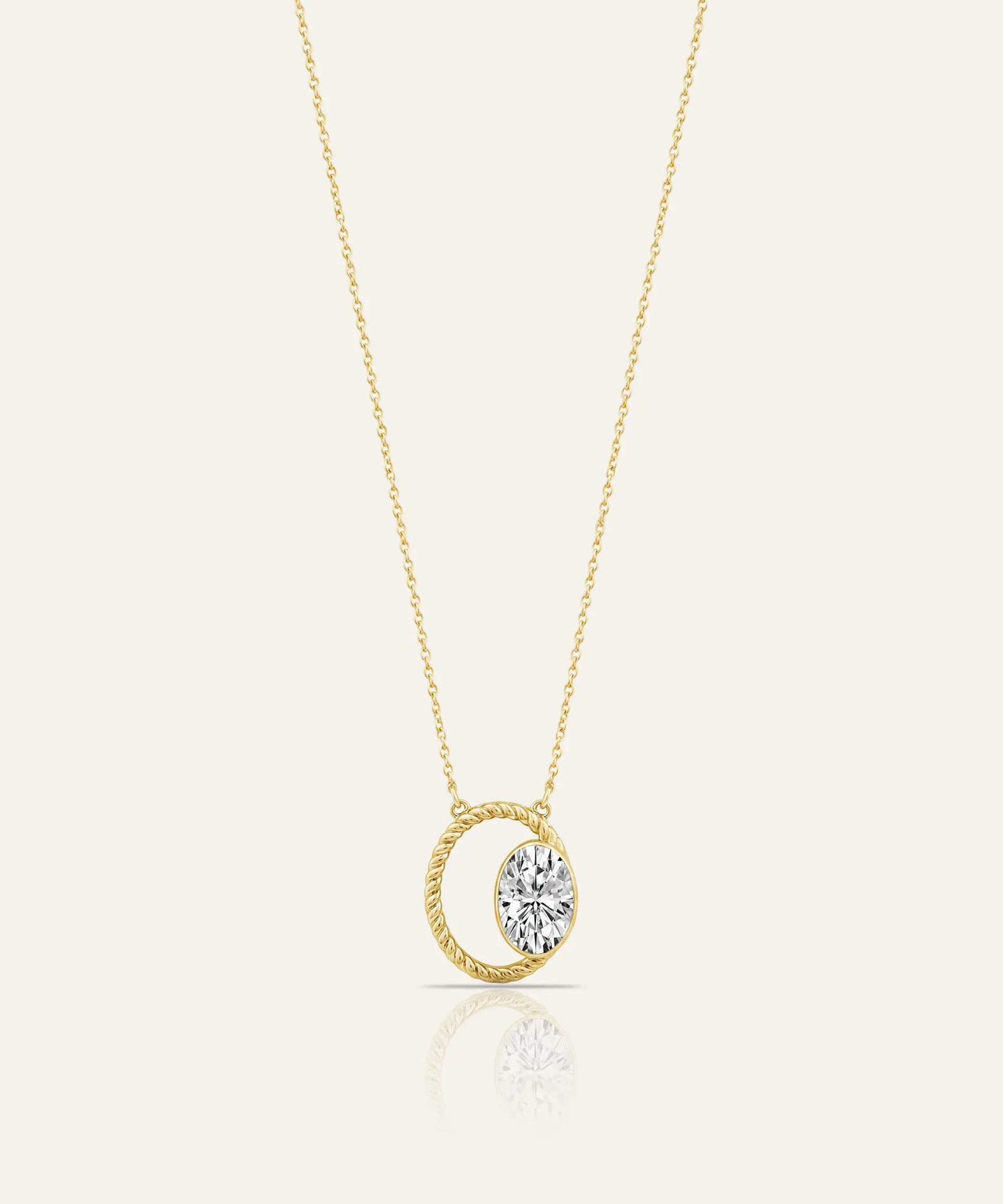 A delicate yellow gold chain necklace with a pendant featuring a twisted oval frame and a central bezel-set clear gemstone, shown on a light cream background with a soft reflection below.