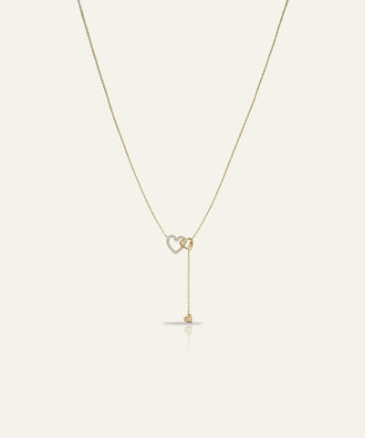 Gold necklace with a heart-shaped pendant on a light beige background