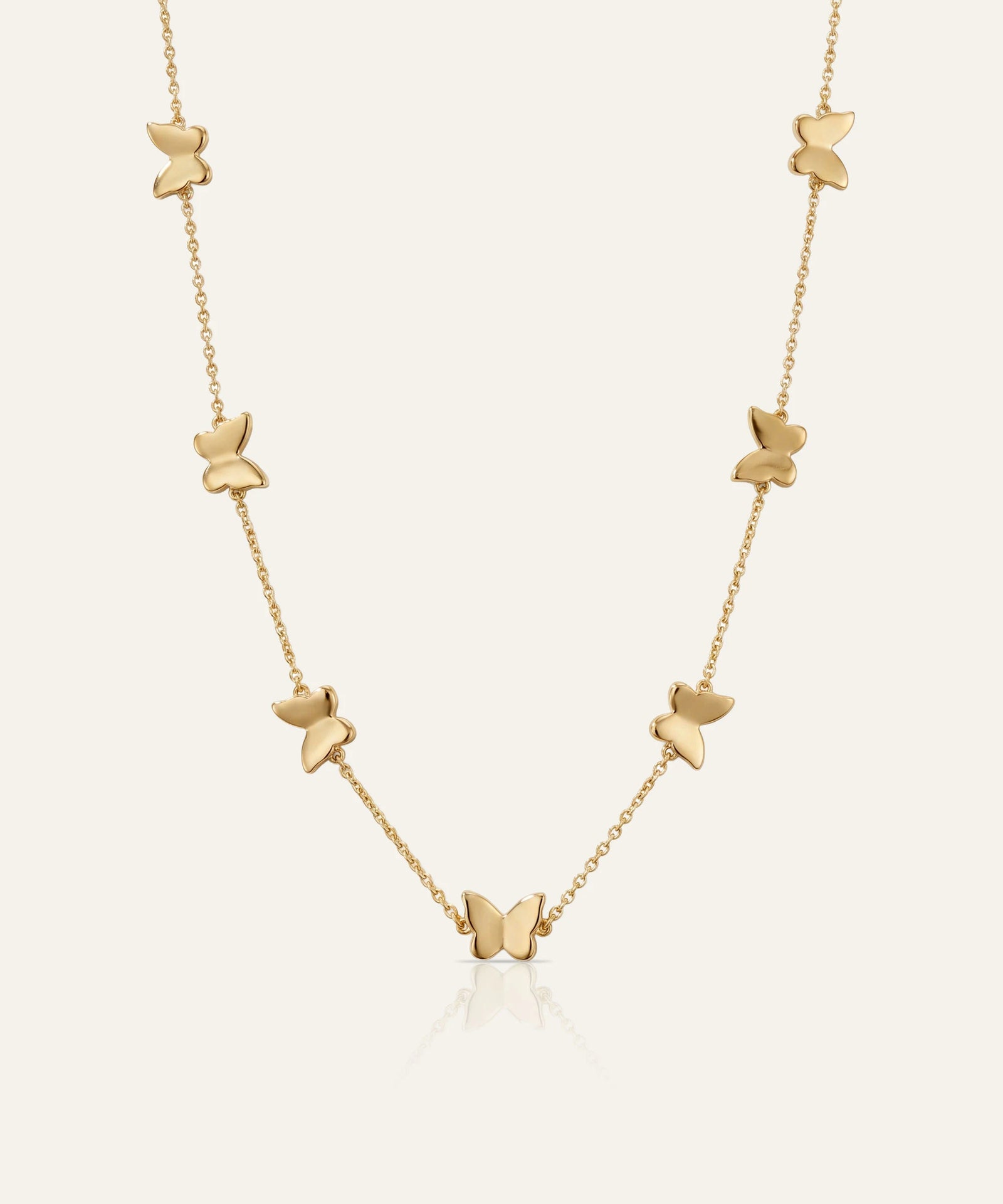 Gold butterfly necklace on a light beige background