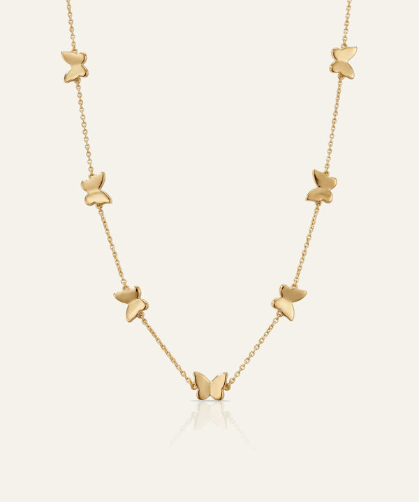 Gold butterfly necklace on a light beige background
