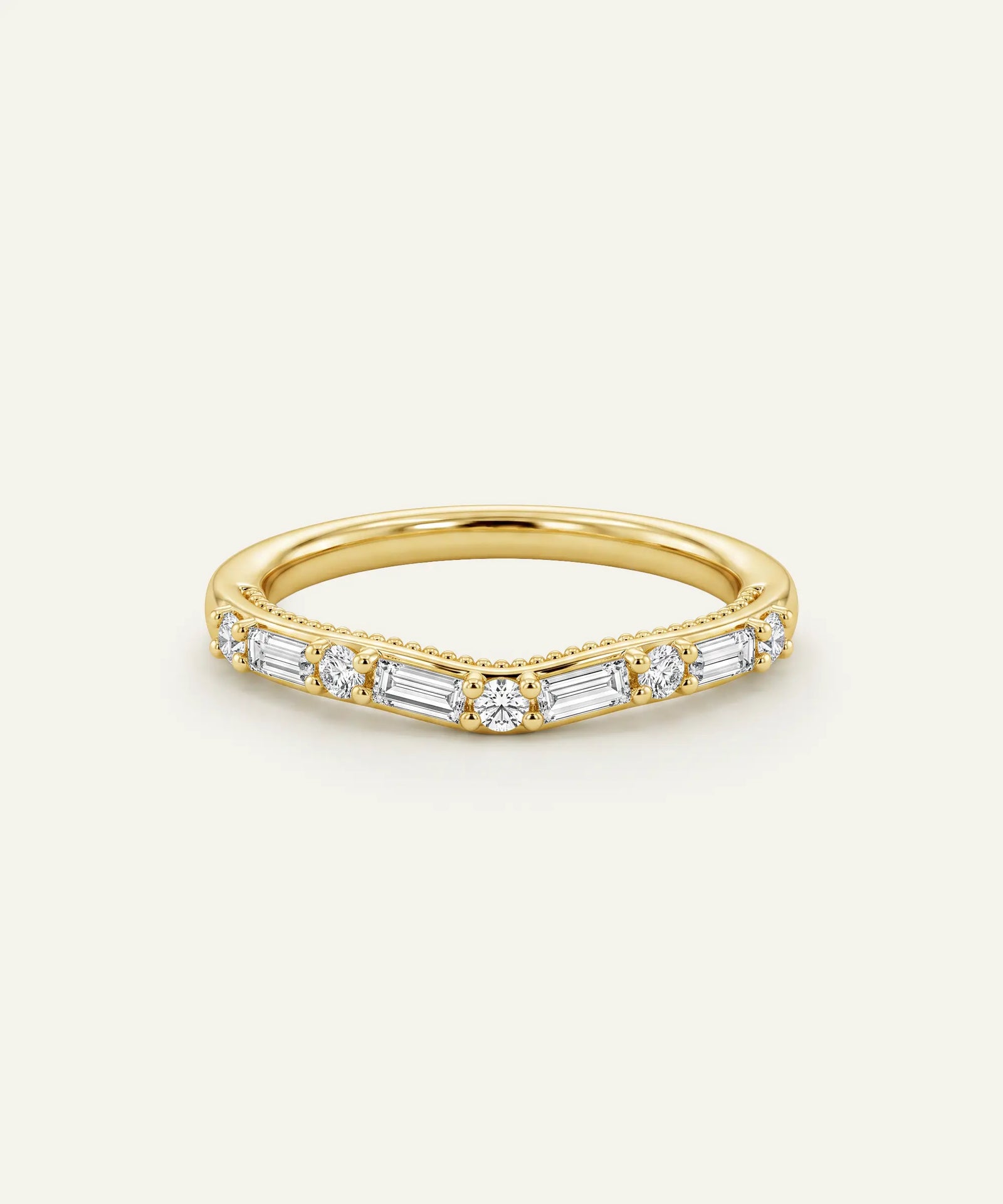 A gold V-shaped band ring featuring baguette and round-cut clear stones, presented on a light cream background.