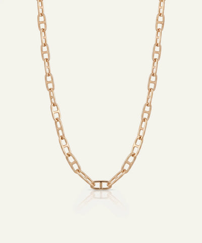 A rose gold paperclip chain necklace displayed on a light cream background with a subtle reflection at the bottom.
