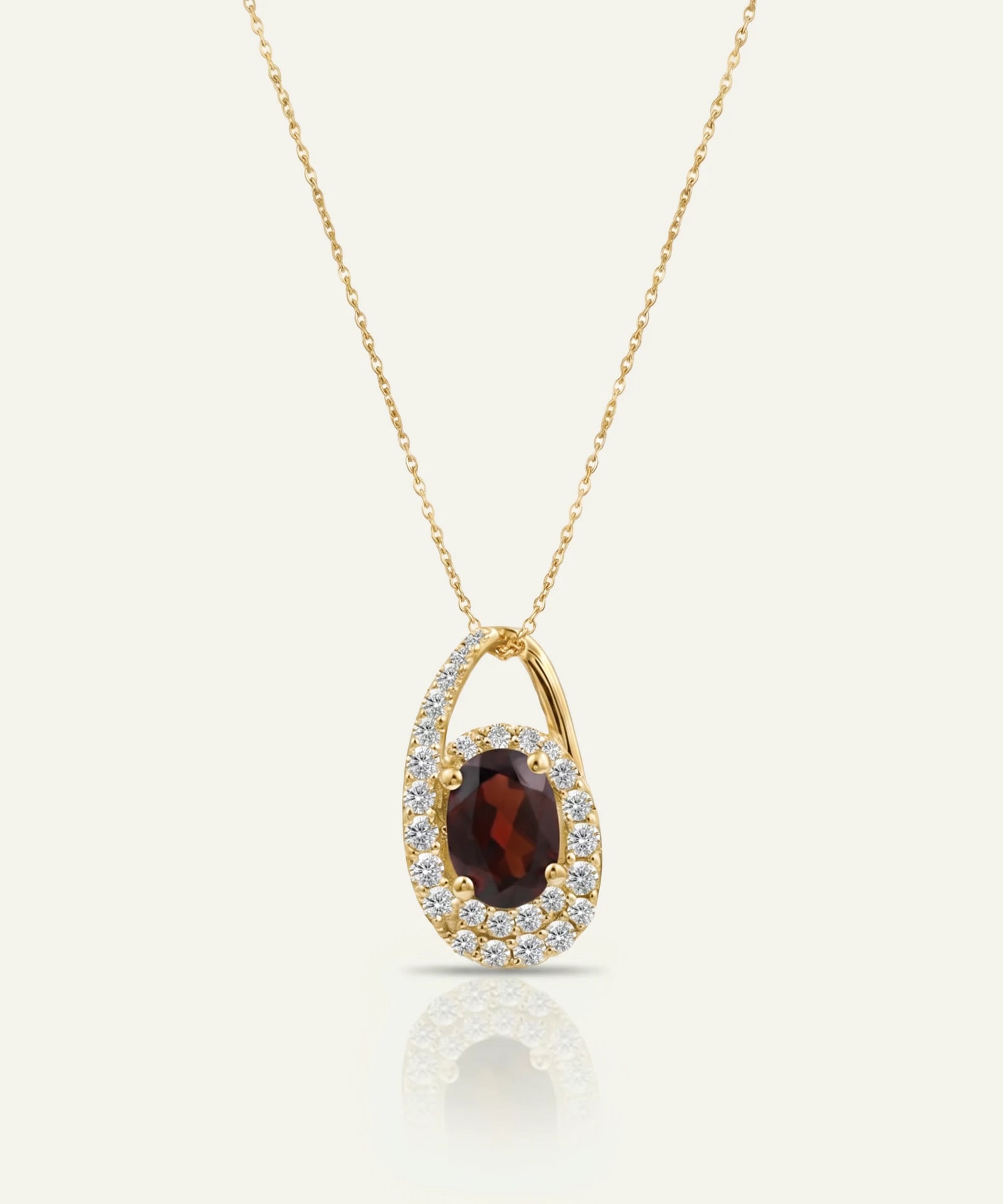 Gold necklace with a pendant featuring a red gemstone on a white background