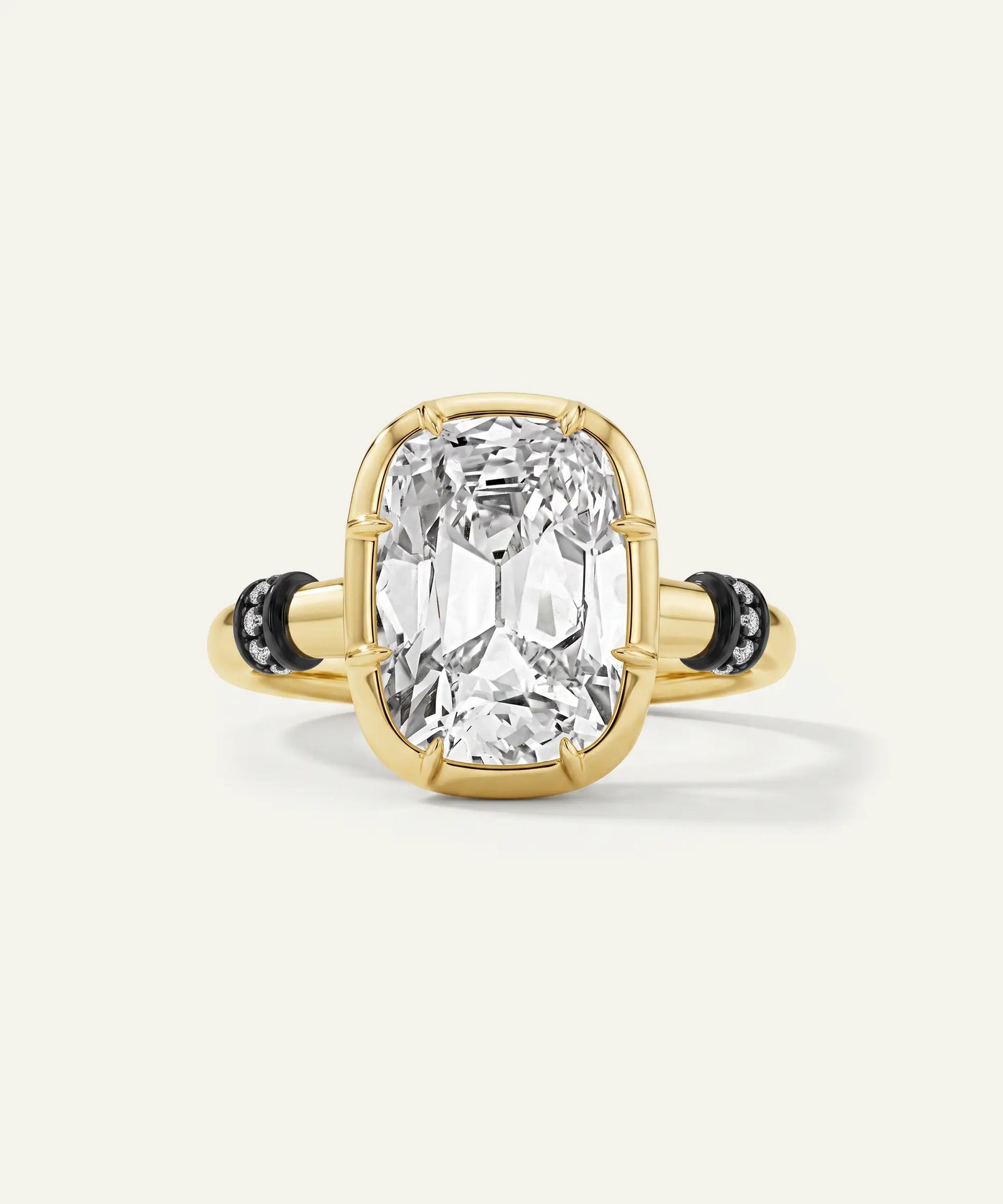 A yellow gold ring featuring a large cushion-cut clear gemstone in a prong setting, accented by small black stones on the band, set against a light cream background.