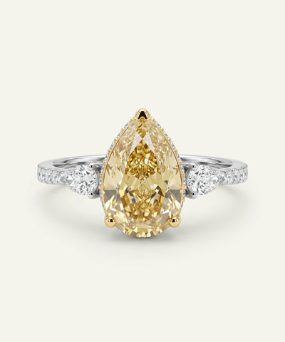 Ring with a pear-shaped yellow diamond and white gemstones on a light gray background