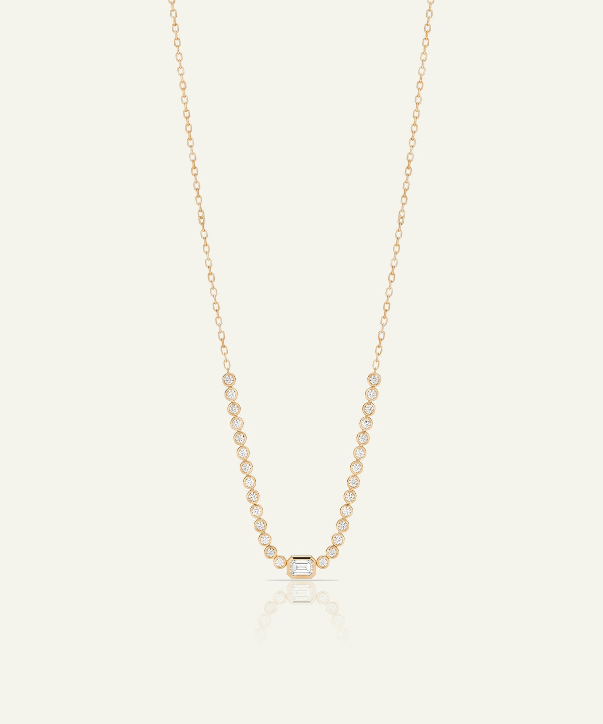 A delicate rose gold chain necklace featuring a central geometric pendant and a row of small clear stones along the chain, displayed on a light cream background with a soft reflection.