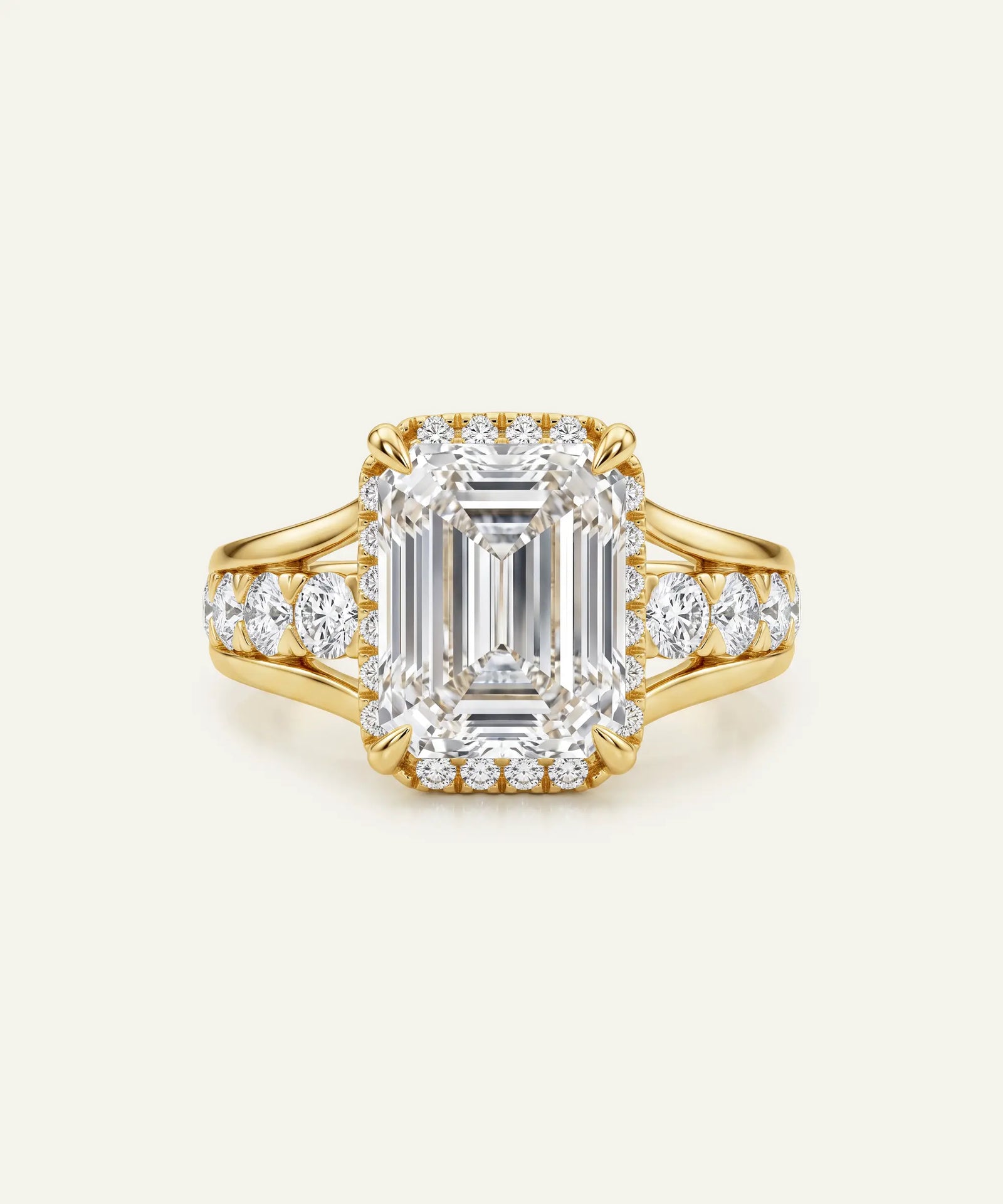 A yellow gold ring featuring a large emerald-cut diamond center stone surrounded by a halo of smaller round diamonds, with additional diamonds set along the shoulders of the band, shown on a light cream background.