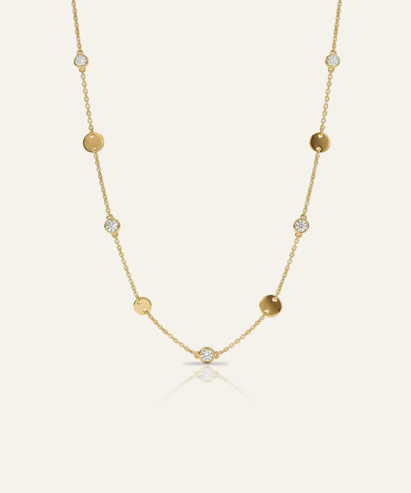 Gold necklace with small round beads and clear stones on a light beige background
