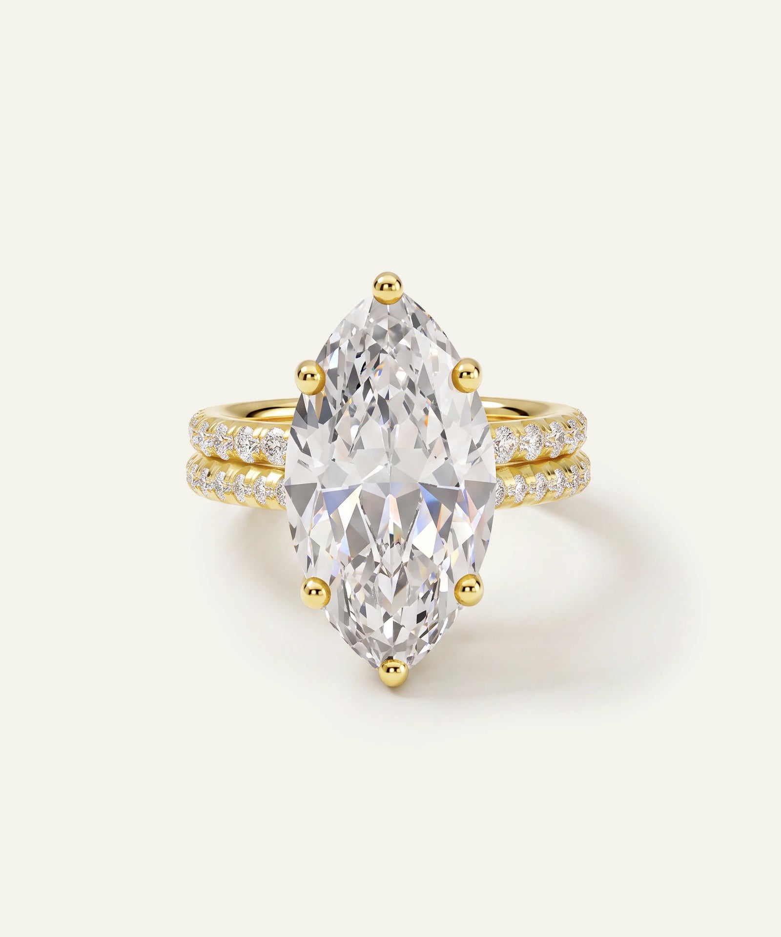 A yellow gold ring featuring a large marquise-cut clear gemstone in a prong setting, with a double-row pavé band accented by small round diamonds, shown on a light cream background.