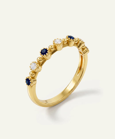 A yellow gold eternity-style ring featuring alternating floral clusters of round-cut blue sapphires and clear round-cut diamonds, set against a clean off-white background.