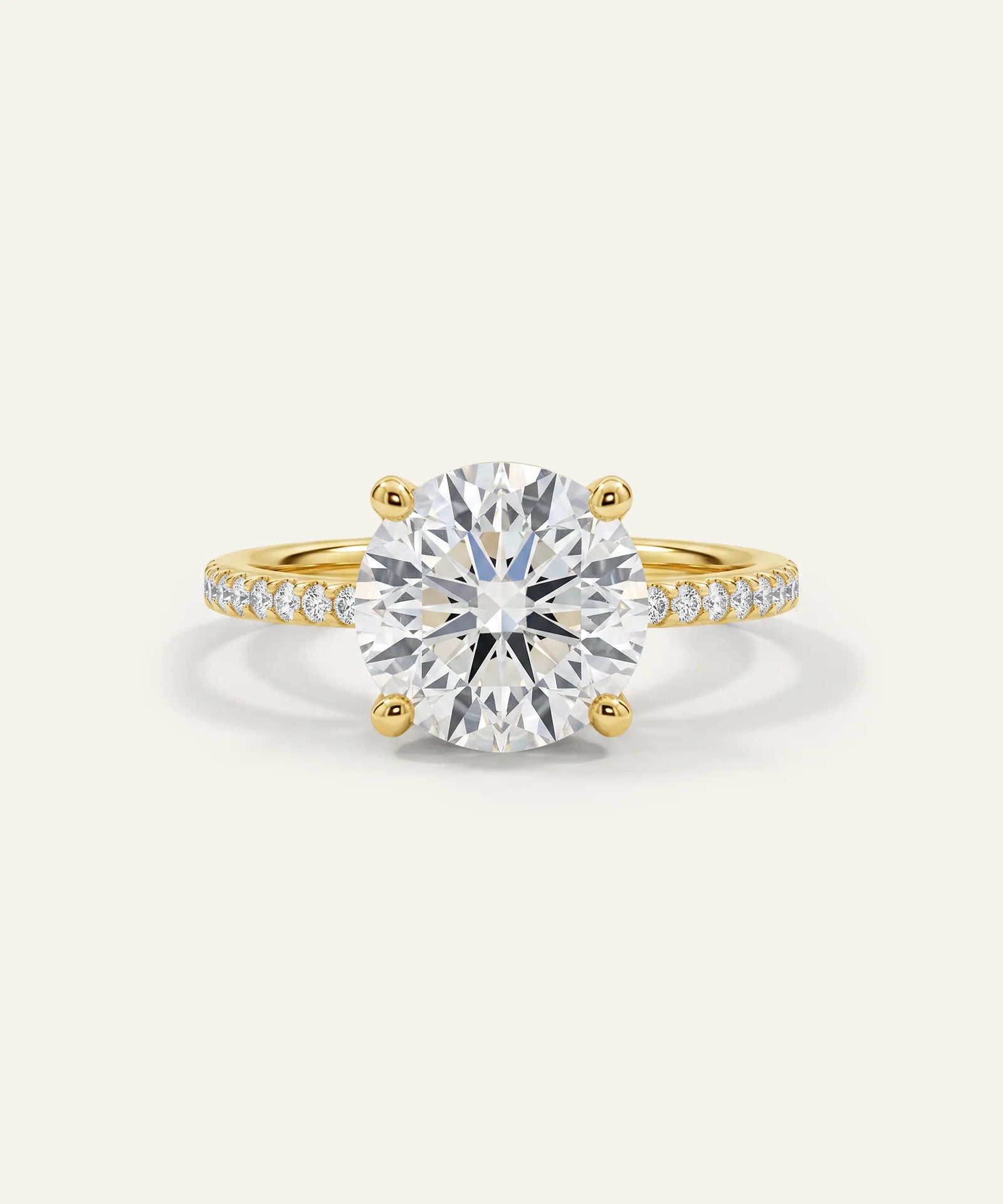 A yellow gold solitaire engagement ring featuring a large round brilliant-cut diamond center stone, with a pavé-set diamond band, shown on a light off-white background.