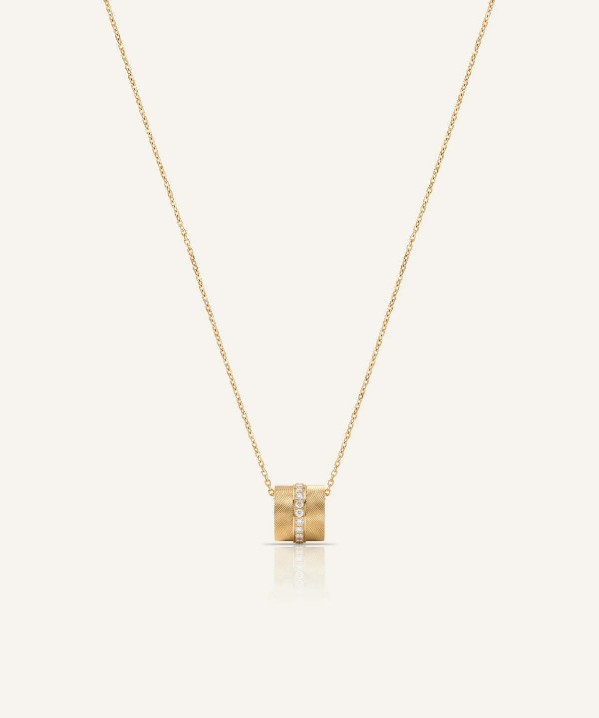 A delicate gold chain necklace with a small cylindrical pendant featuring a central row of clear stones, displayed against a solid off-white background.