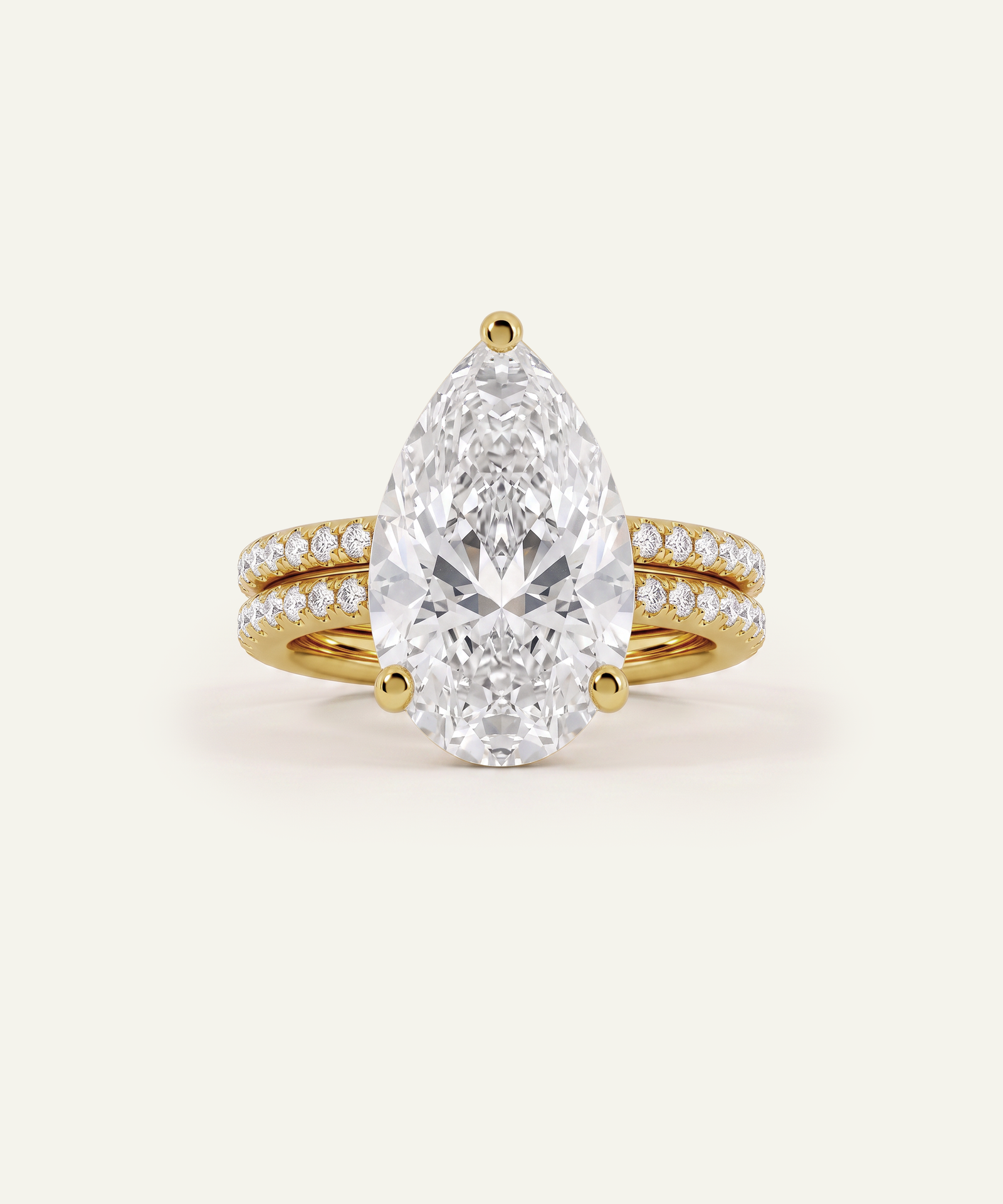 A pear-cut diamond engagement ring with a yellow gold band accented by pavé diamonds, shown on a light cream background.