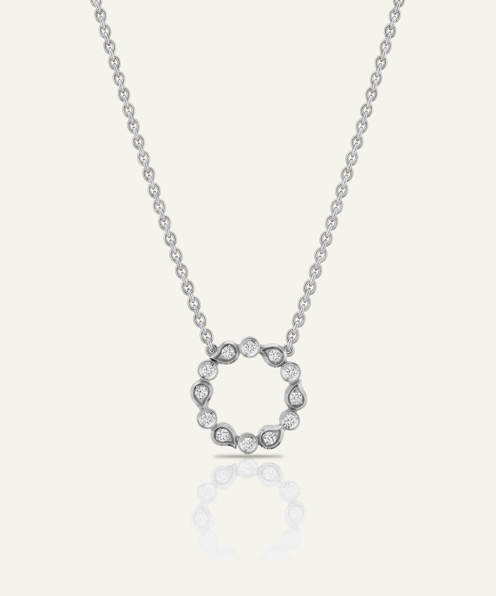 A silver-toned necklace with a circular open pendant set with small clear stones, displayed on a light cream background with a soft reflection below.