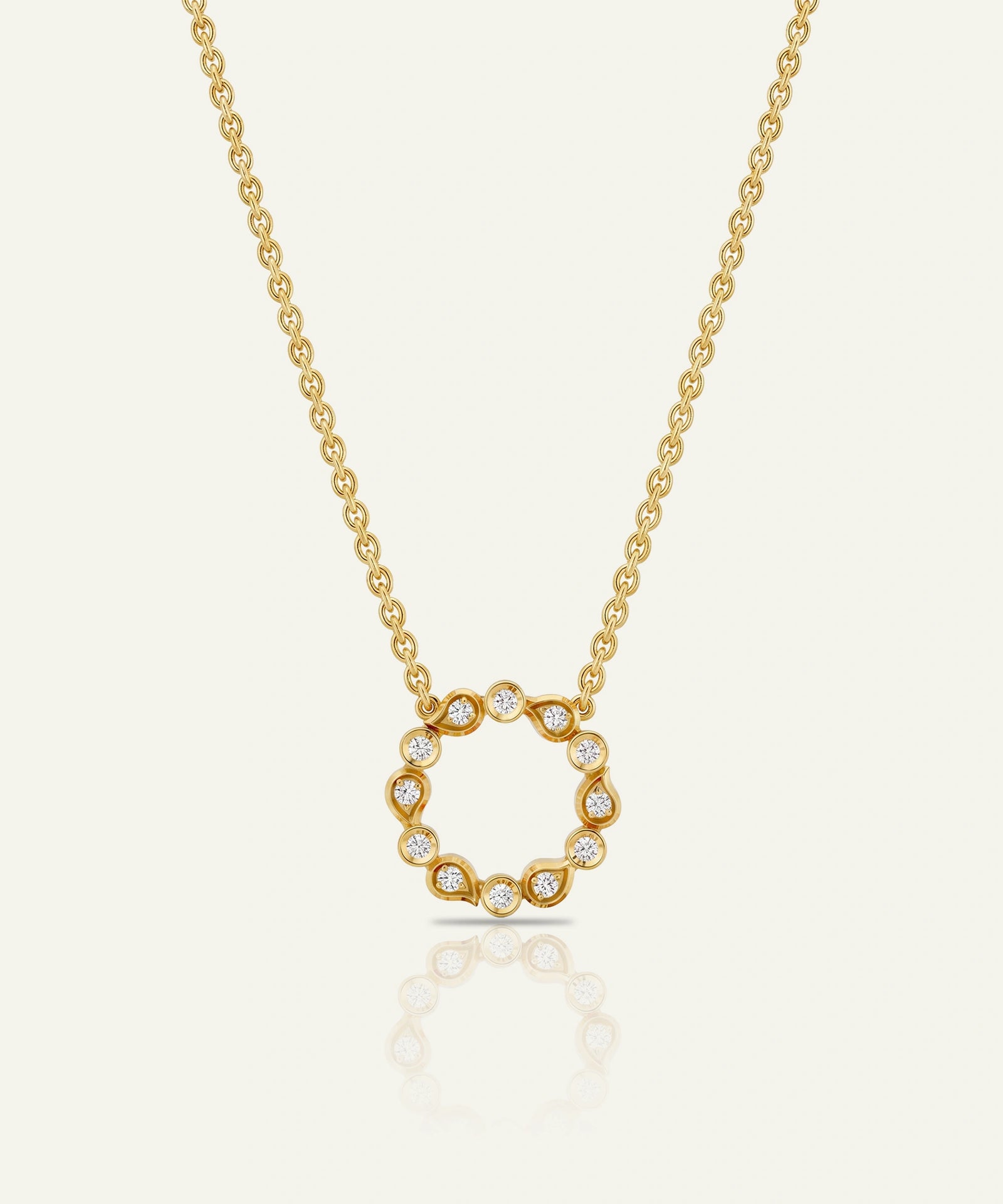 A delicate gold chain necklace featuring a circular pendant with small clear stones set along the edge, displayed against a light cream background with a soft reflection below.