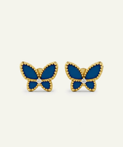 A pair of gold butterfly stud earrings with deep blue enamel wings and a small clear stone at the center, displayed on a light cream background.