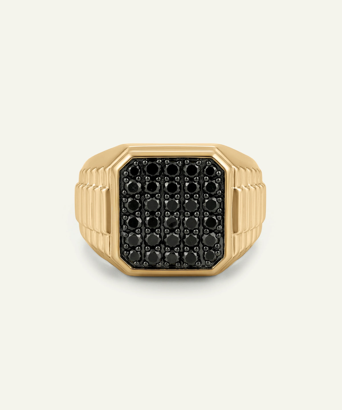 A gold signet ring featuring a black pavé face with small circular stones, photographed against a light off-white background.
