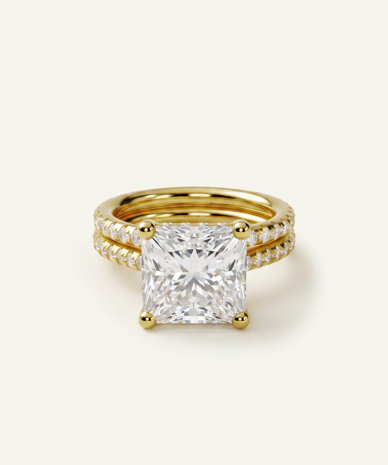 A yellow gold ring set featuring a large princess-cut diamond center stone with a pave diamond band, photographed on a clean off-white background.