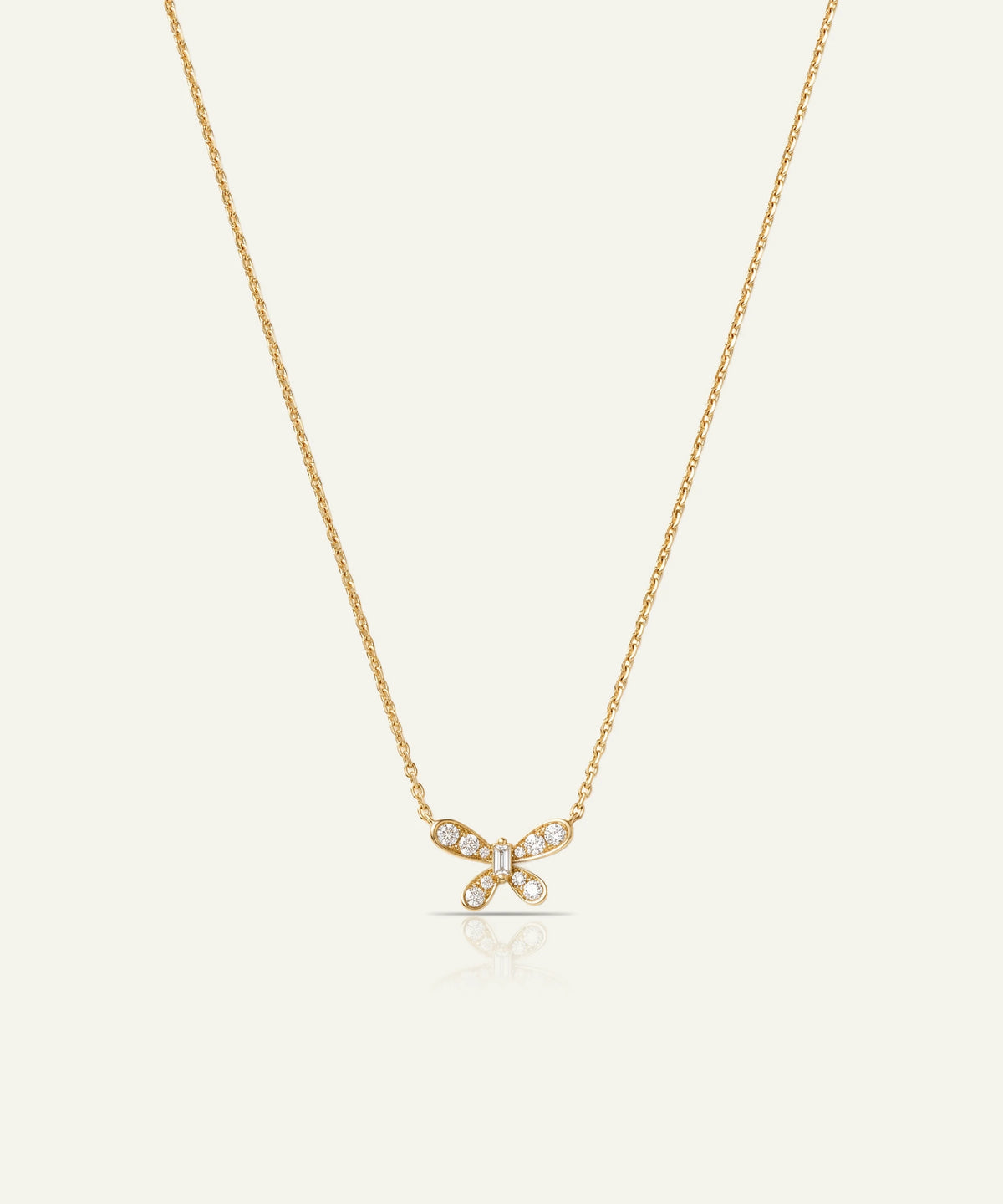 A delicate gold chain necklace featuring a small bow-shaped pendant adorned with clear pavé-set stones, displayed against a solid off-white background.