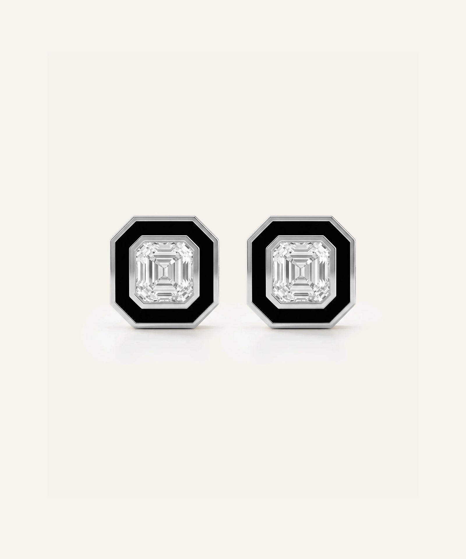 A pair of octagonal stud earrings with a silver-toned metal frame, a black enamel border, and a central clear emerald-cut diamond, shown on a light cream background.