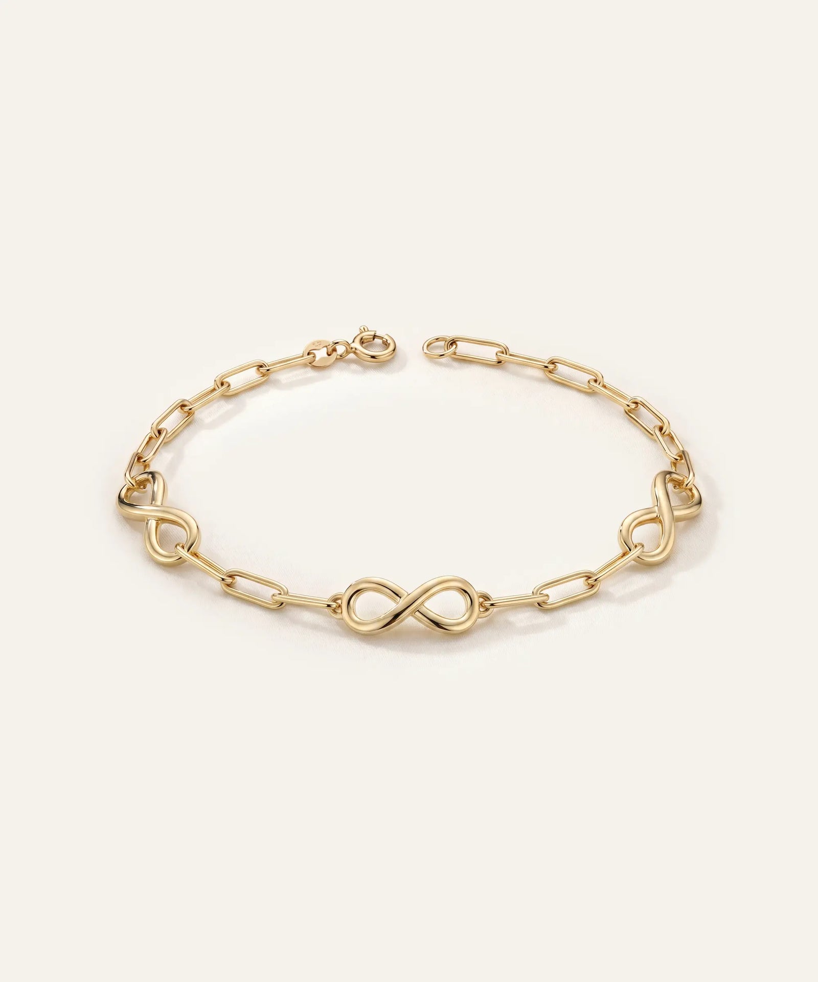Gold bracelet with infinity symbol links on a light beige background