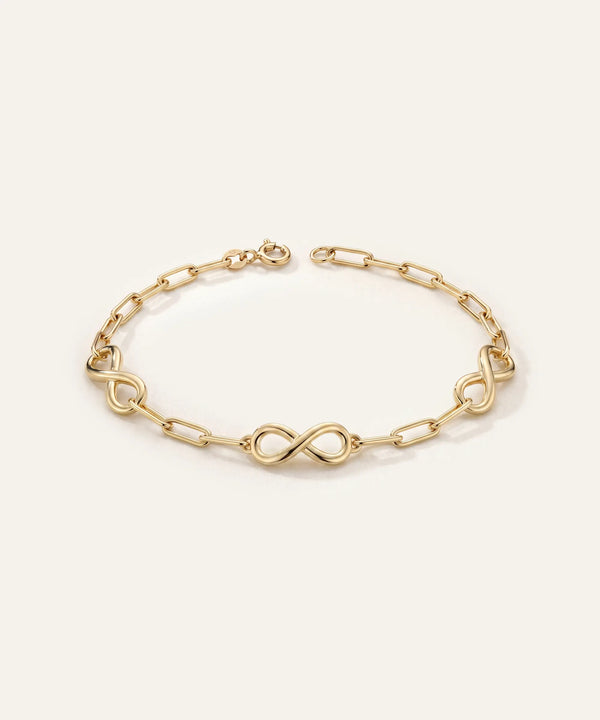 Gold bracelet with infinity symbol links on a light beige background