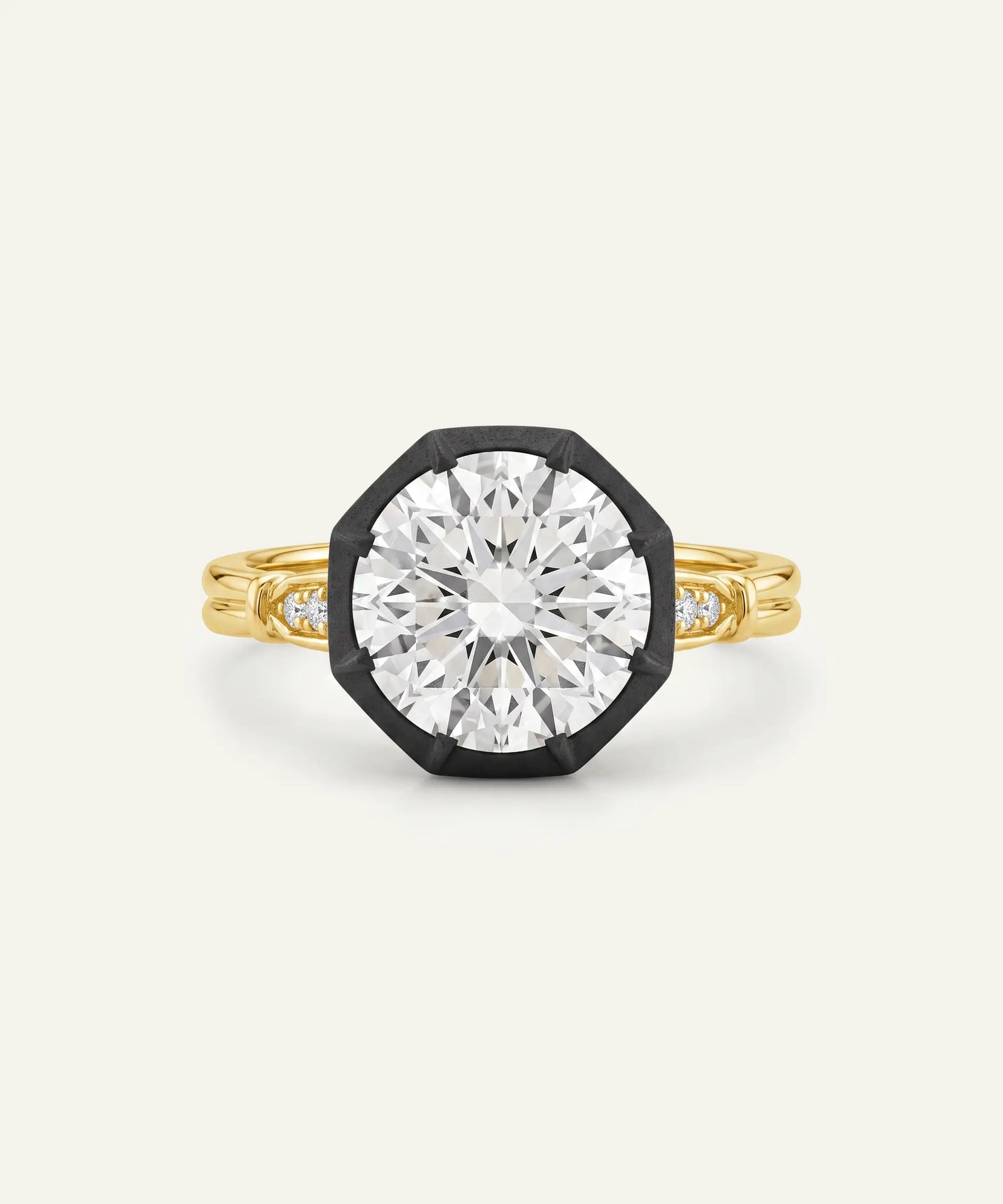A yellow gold octagonal ring with a large clear round-cut center stone and small side stones, set in a black bezel-like frame on a light cream background.
