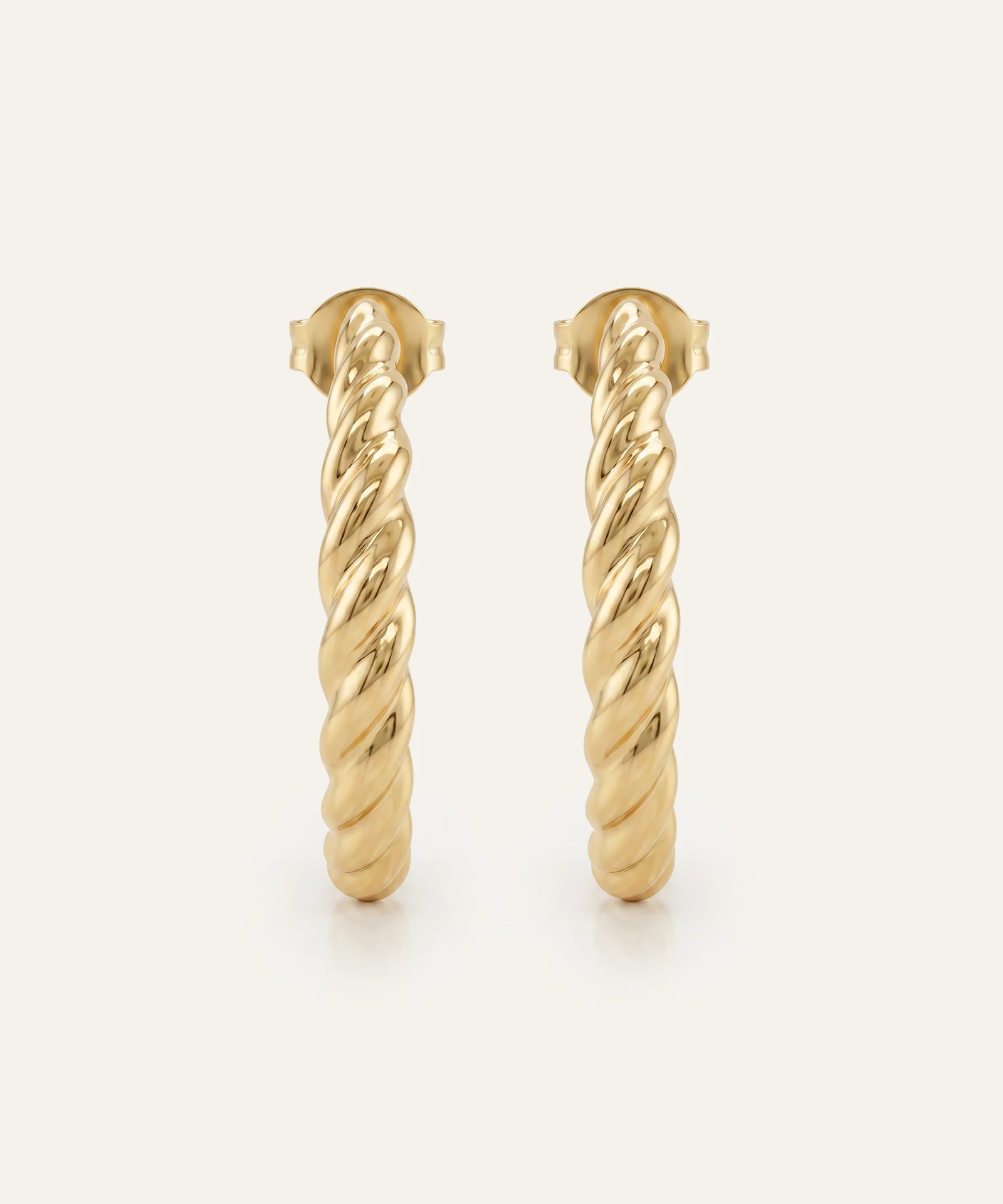 Gold hoop earrings with twisted design on a light beige background