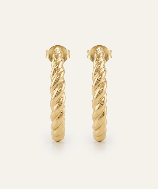 Gold hoop earrings with twisted design on a light beige background