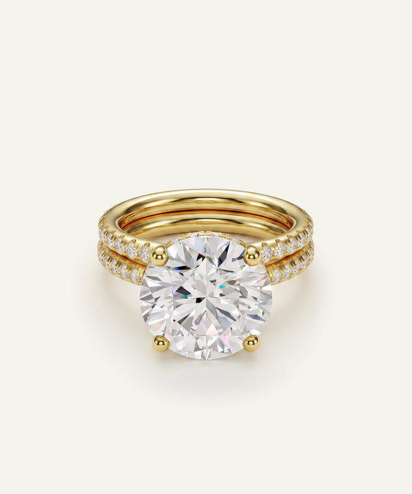 A gold engagement ring with a large round brilliant-cut center stone and a double-row pavé band, shown on a clean off-white background.