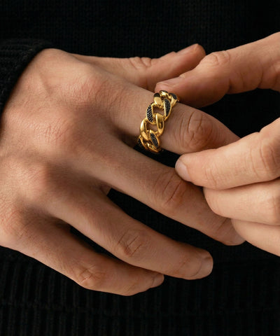 Close-up of hands wearing a gold chain ring on a black background - alternate view