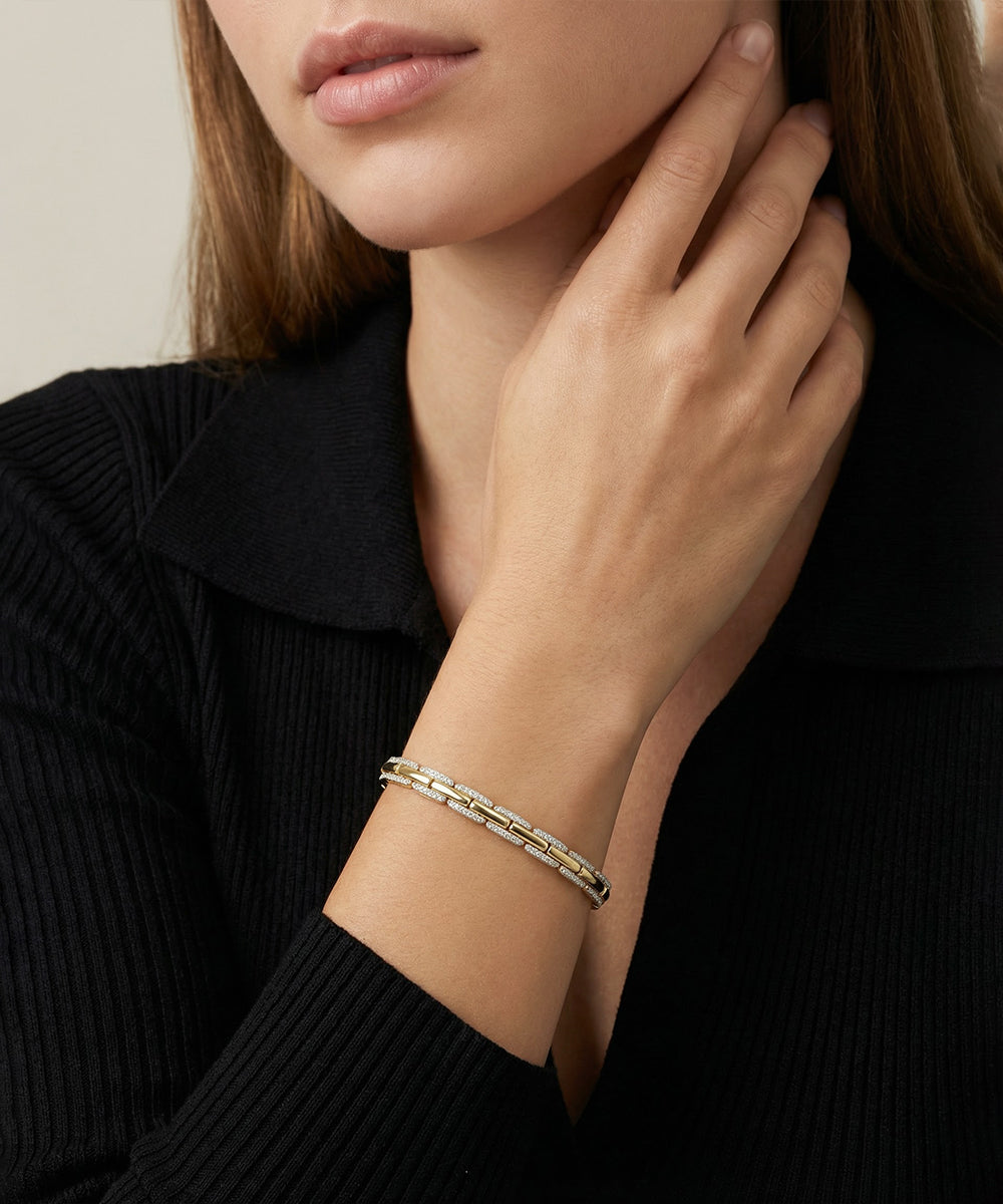 Close-up of a person wearing a gold bracelet on a plain background
