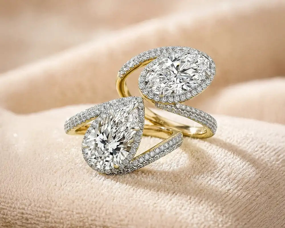 Yellow gold two-stone pear-cut diamond ring on a neutral beige background.