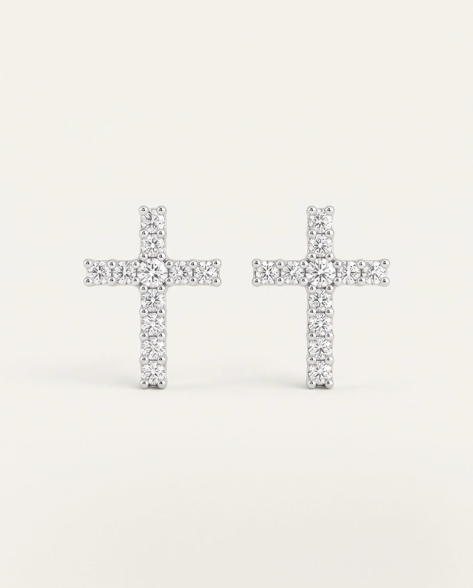 A pair of silver cross stud earrings paved with small clear stones, set against a plain off-white background.