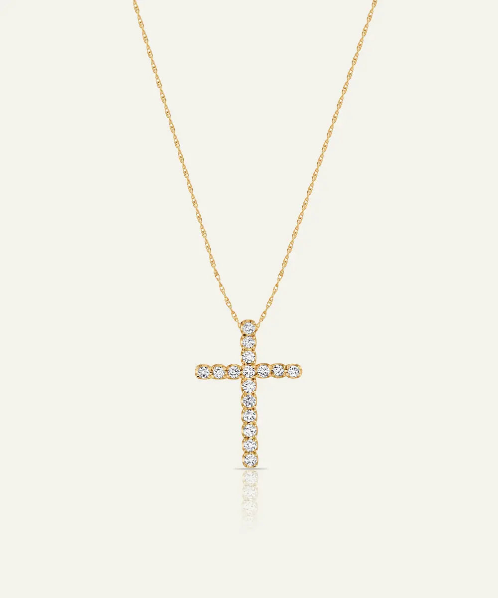 Yellow gold cross pendant set with round clear diamonds on a fine chain, displayed on an off-white background.