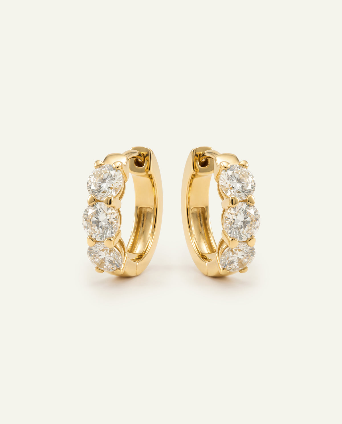 Pair of yellow gold huggie hoop earrings set with brilliant round diamonds on an off-white background.